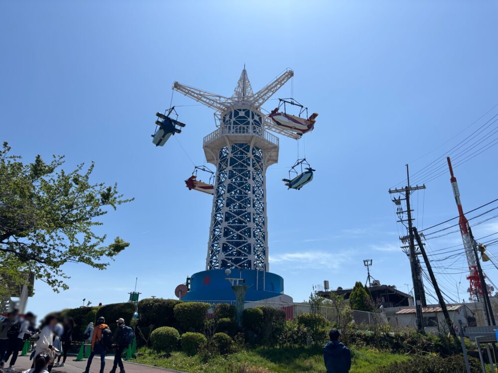 The iconic Flying Tower ride at Ikoma Sanjo Amusement Park, with colorful airplane-shaped gondolas spinning under a clear blue sky