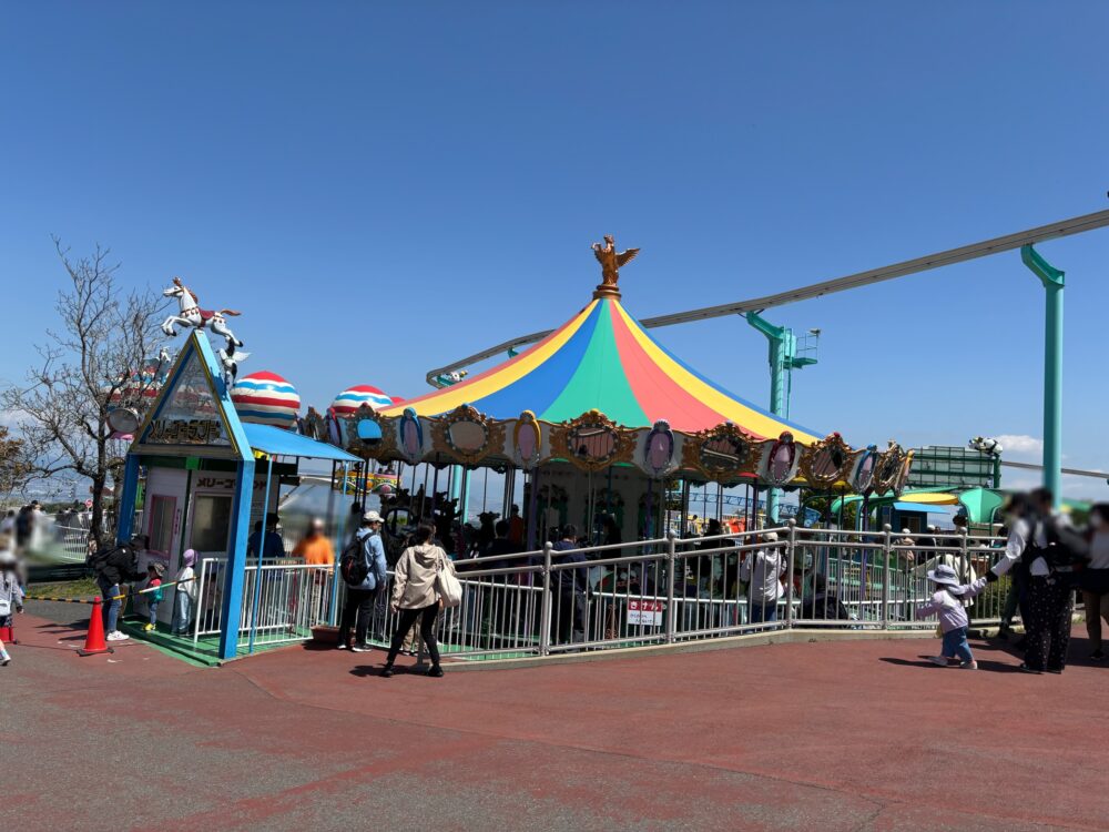 Colorful merry-go-round ride at Ikoma Sanjo Amusement Park, with families and children enjoying a sunny day