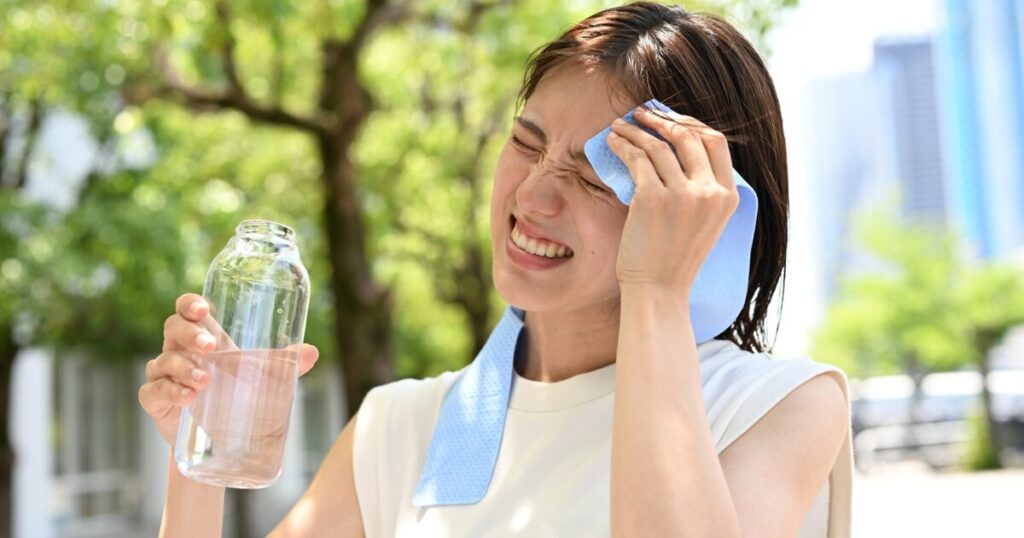 汗をかいた女性がタオルで汗を拭きながら片手に水を持っている様子