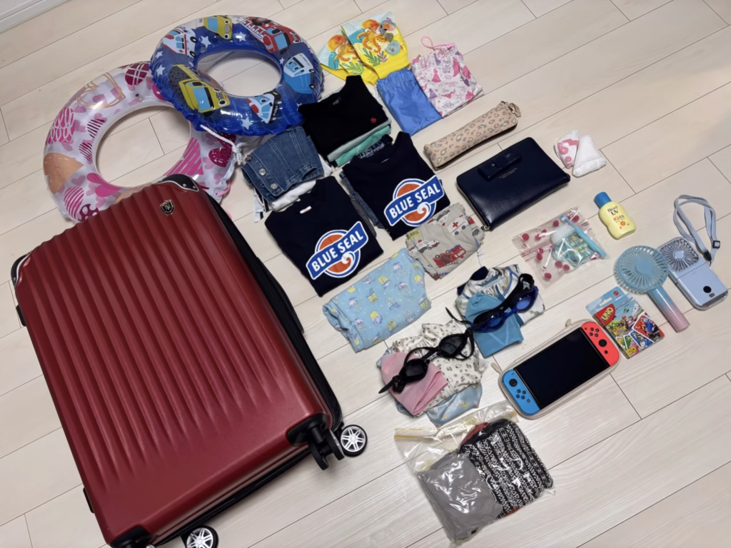 子連れ沖縄旅行の持ち物（子ども）一式：スーツケース、浮き輪、子ども服、日焼け止め、ハンディ扇風機、水着、ゴーグル、switch、ウノ、歯磨き、折り畳み傘、パジャマを並べた様子