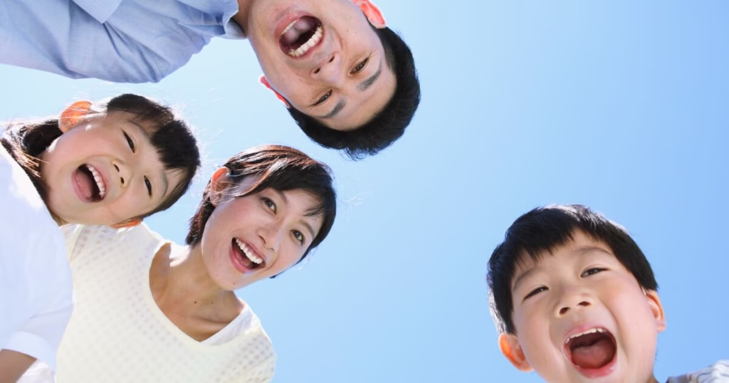 青空の下で家族4人が口を開けて仲良くしている様子