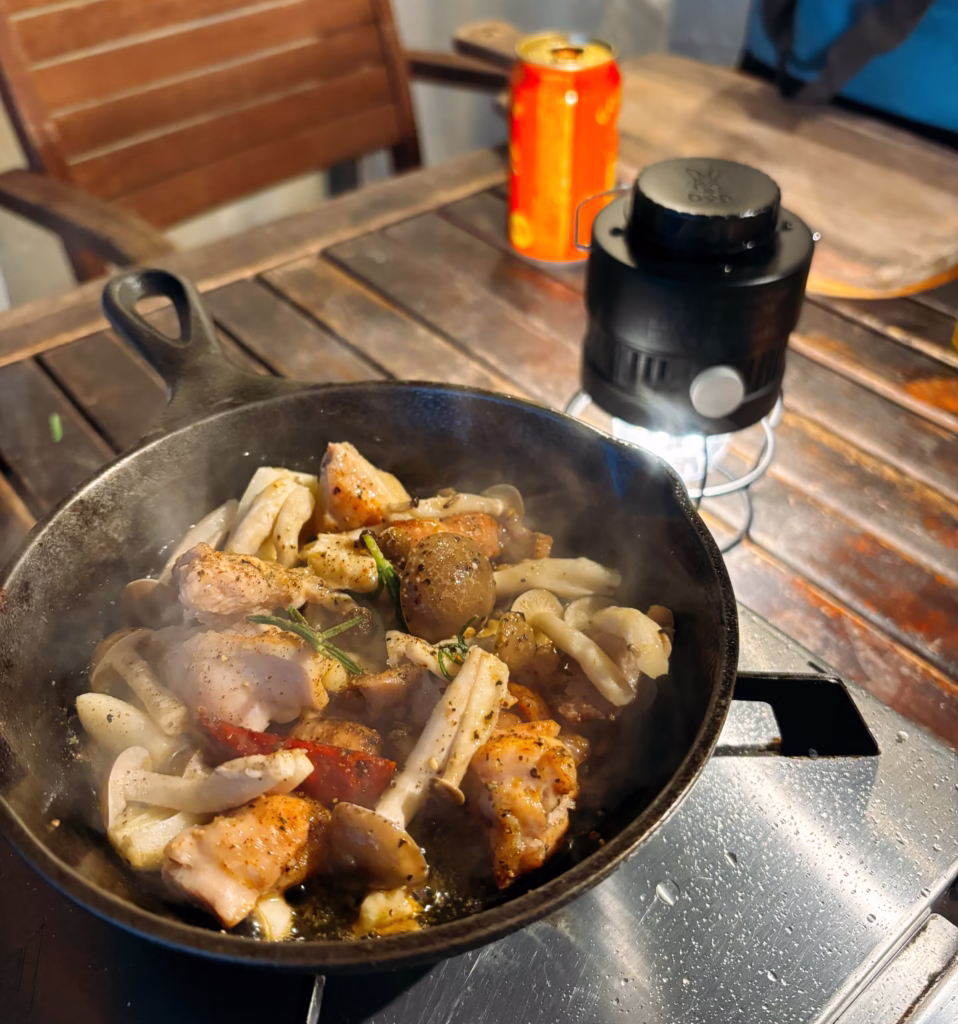 京都るり渓GLAXのテント前で料理をする様子。スキレットに鶏肉、きのこ、鷹の爪、ローズマリーを炒めた料理。